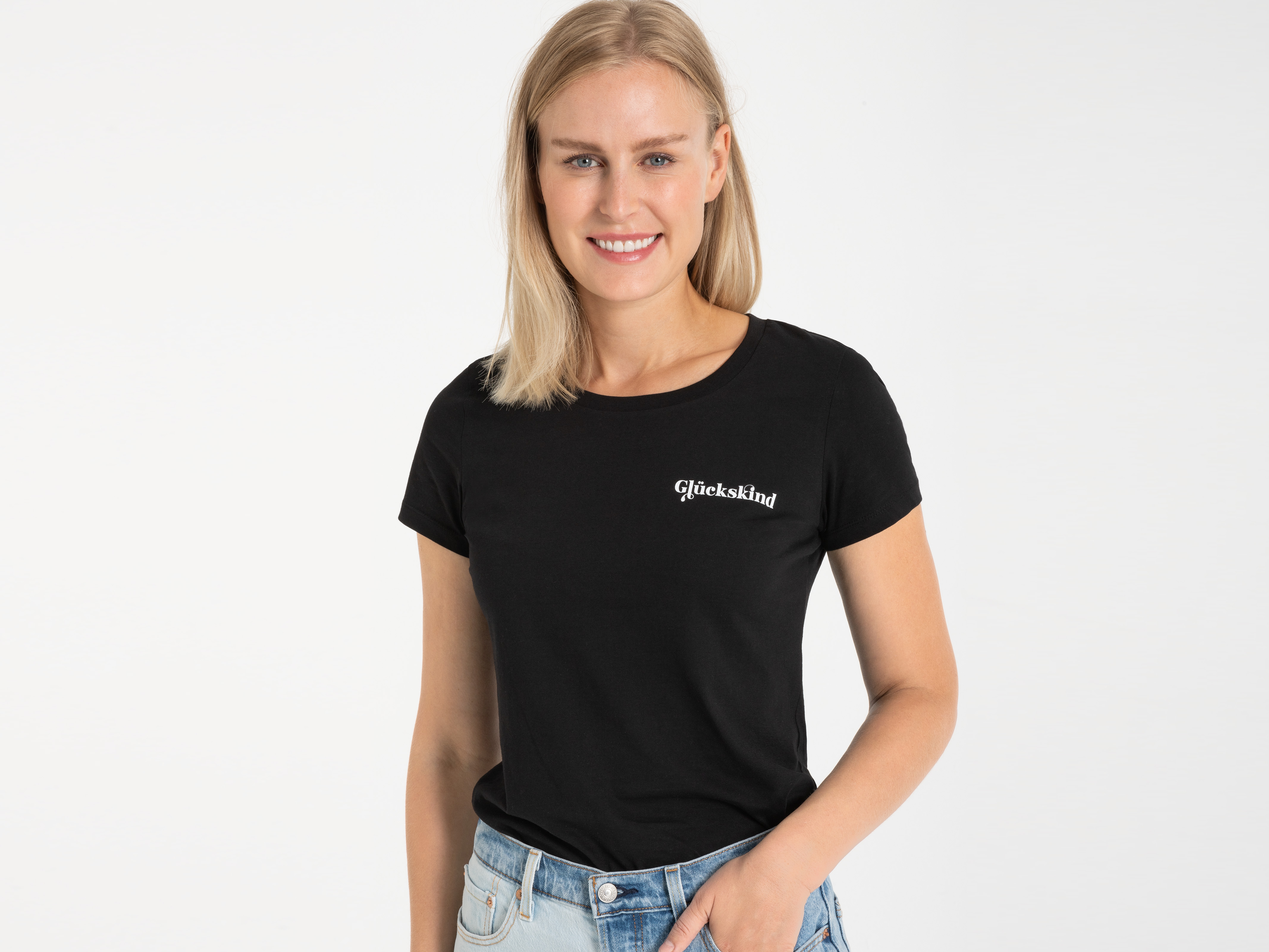Frau im schwarzen T-Shirt mit kleinem weißen Logo, lächelt in die Kamera – freundlicher, alltagstauglicher Stil.