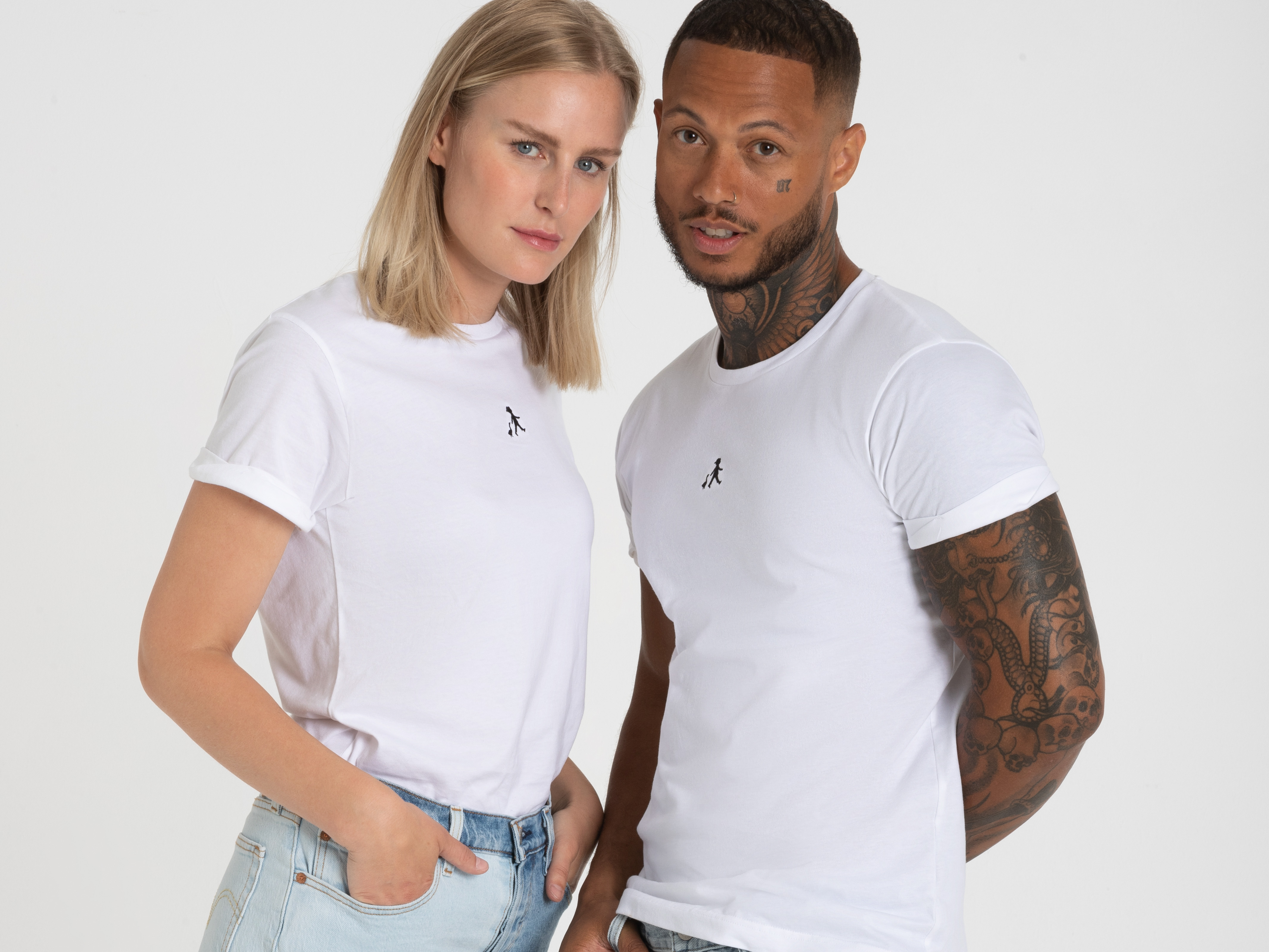 Zwei Personen stehen nebeneinander und blicken frontal in die Kamera. Die Frau trägt ein kurzes weißes T-Shirt, der Mann auch.