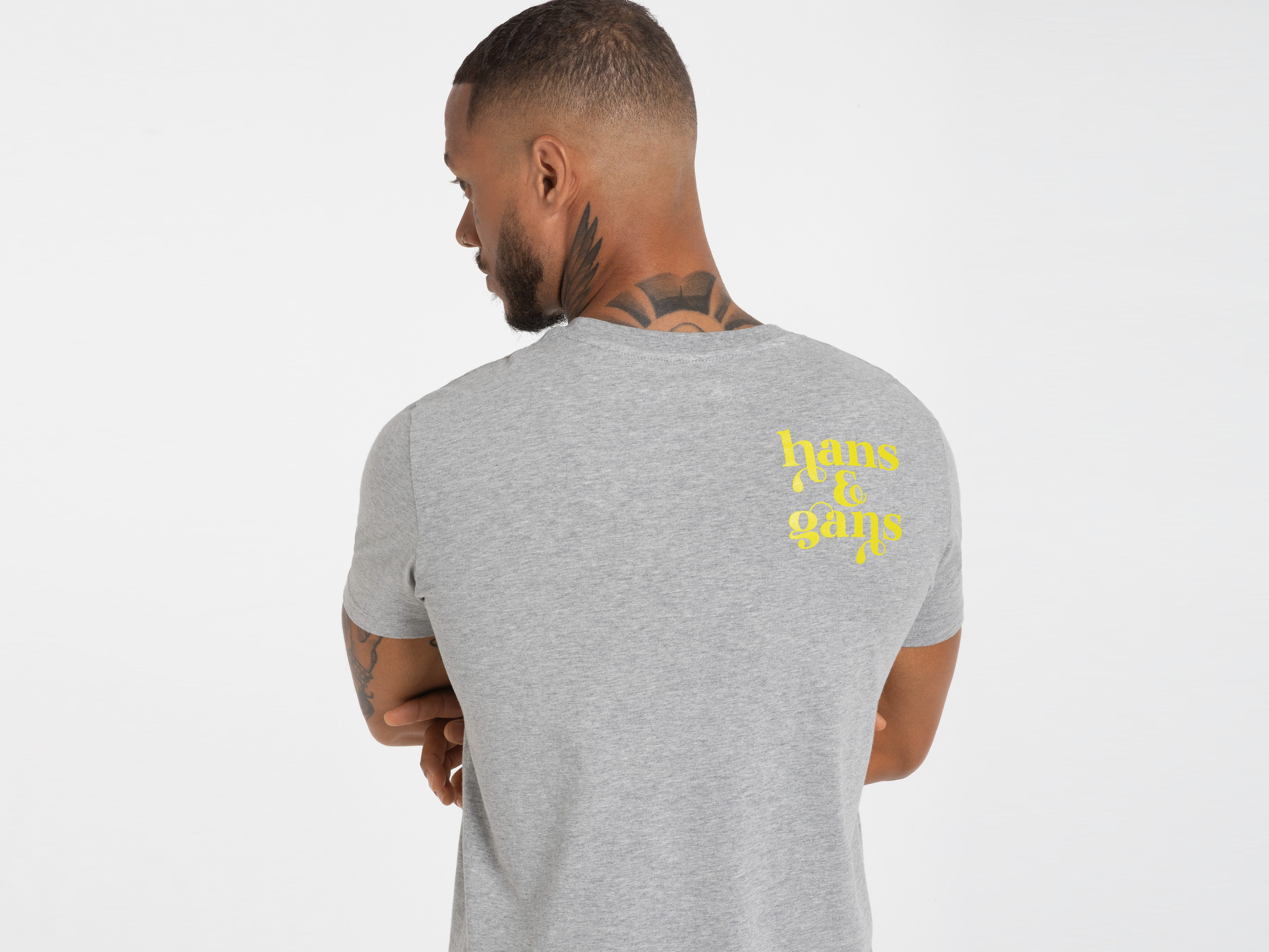 Rückansicht eines Mannes mit verschränkten Armen, Shirt mit gelbem Print – starker Rückenauftritt