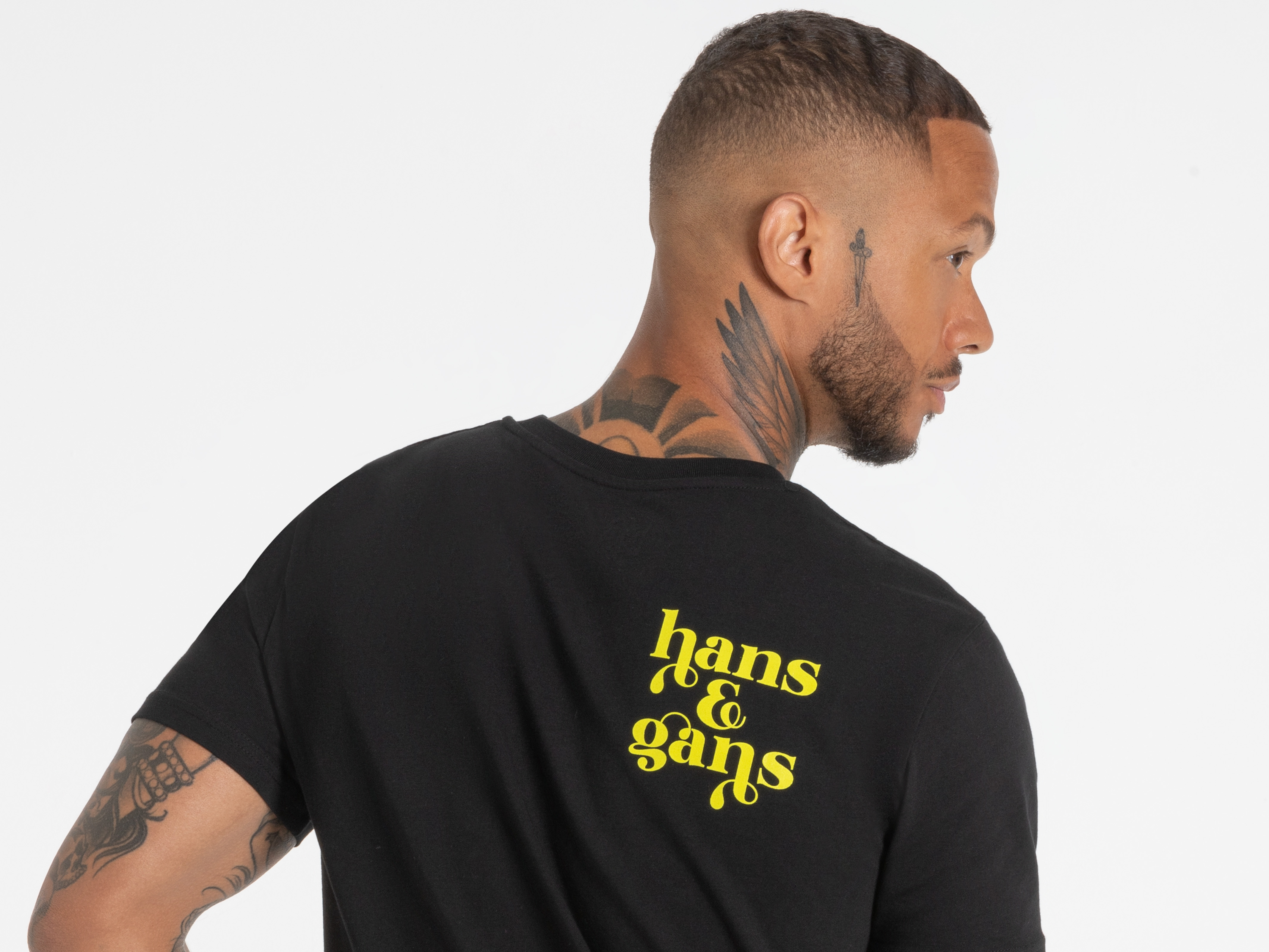 Rückansicht eines schwarzen T-Shirts mit gelbem Schriftzug ‚Hans im Glück‘ – stylisch und markant.