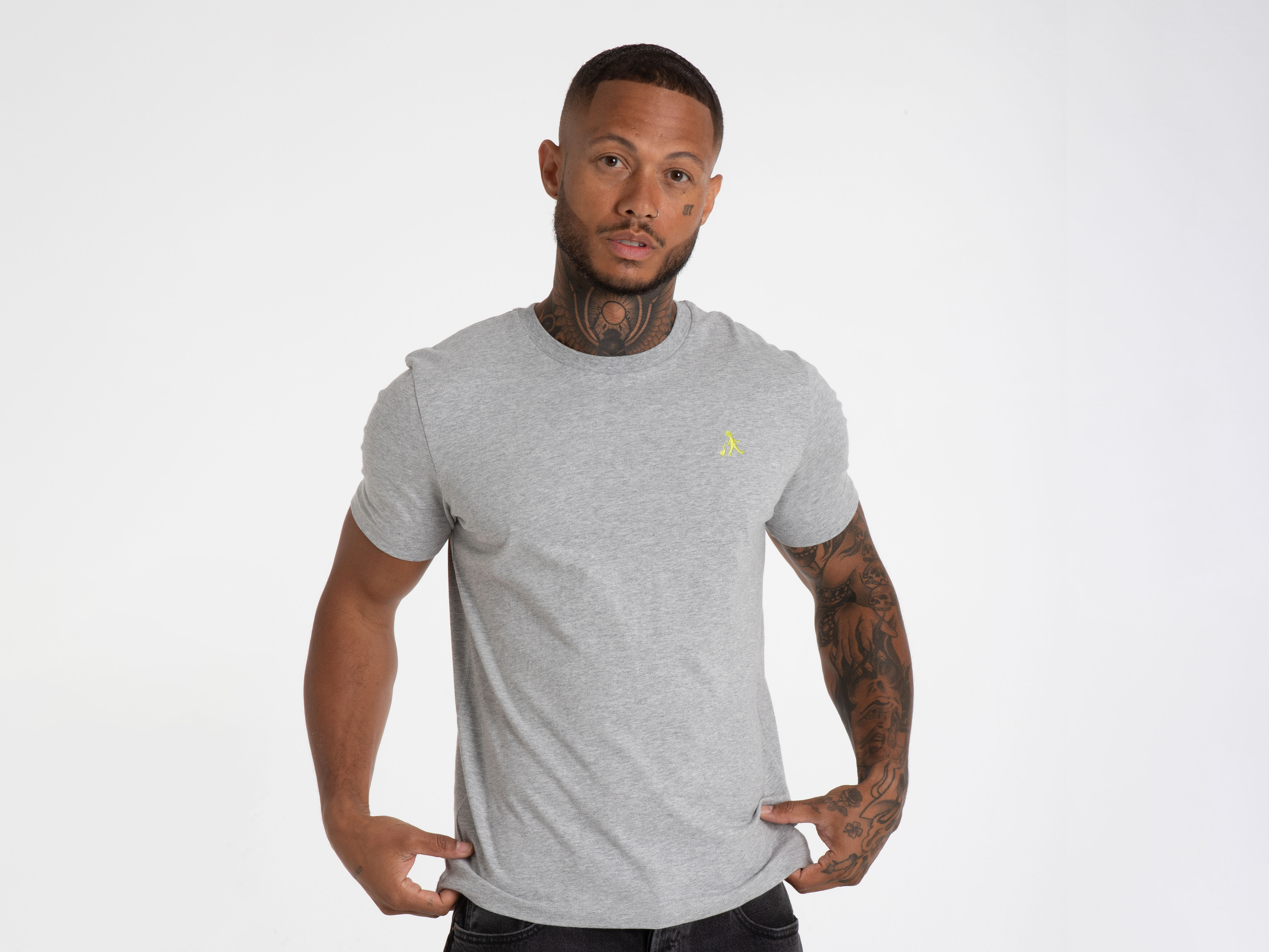Ein Mann trägt ein graues T-Shirt mit kleinem Logoaufdruck. Figurbetont geschnitten, neutraler Hintergrund – modische Basicwear.