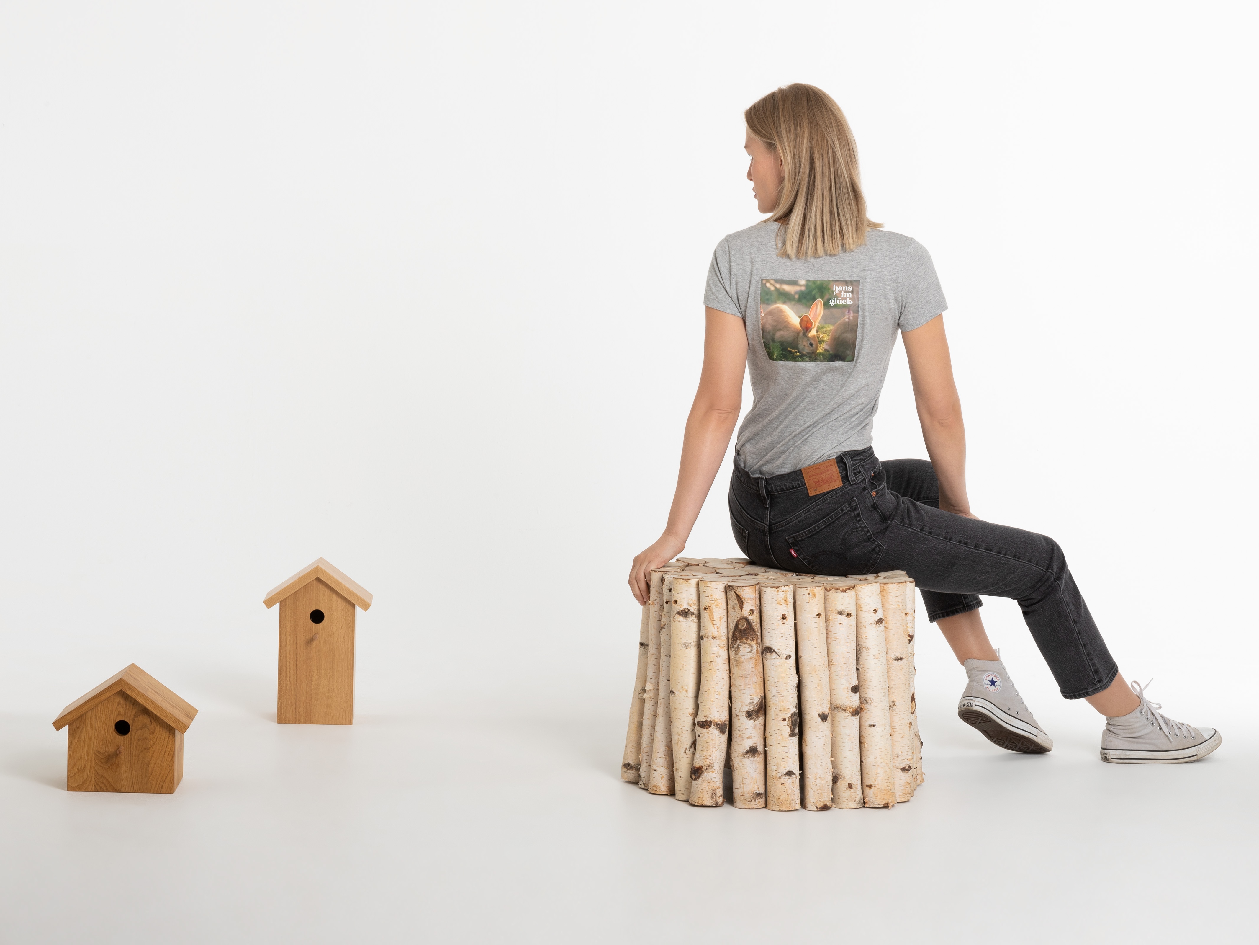 Frau sitzt auf Holzstamm mit Blick nach hinten, trägt graues T-Shirt mit gelbem Logo – modernes Shirt mit entspannter Ausstrahlung