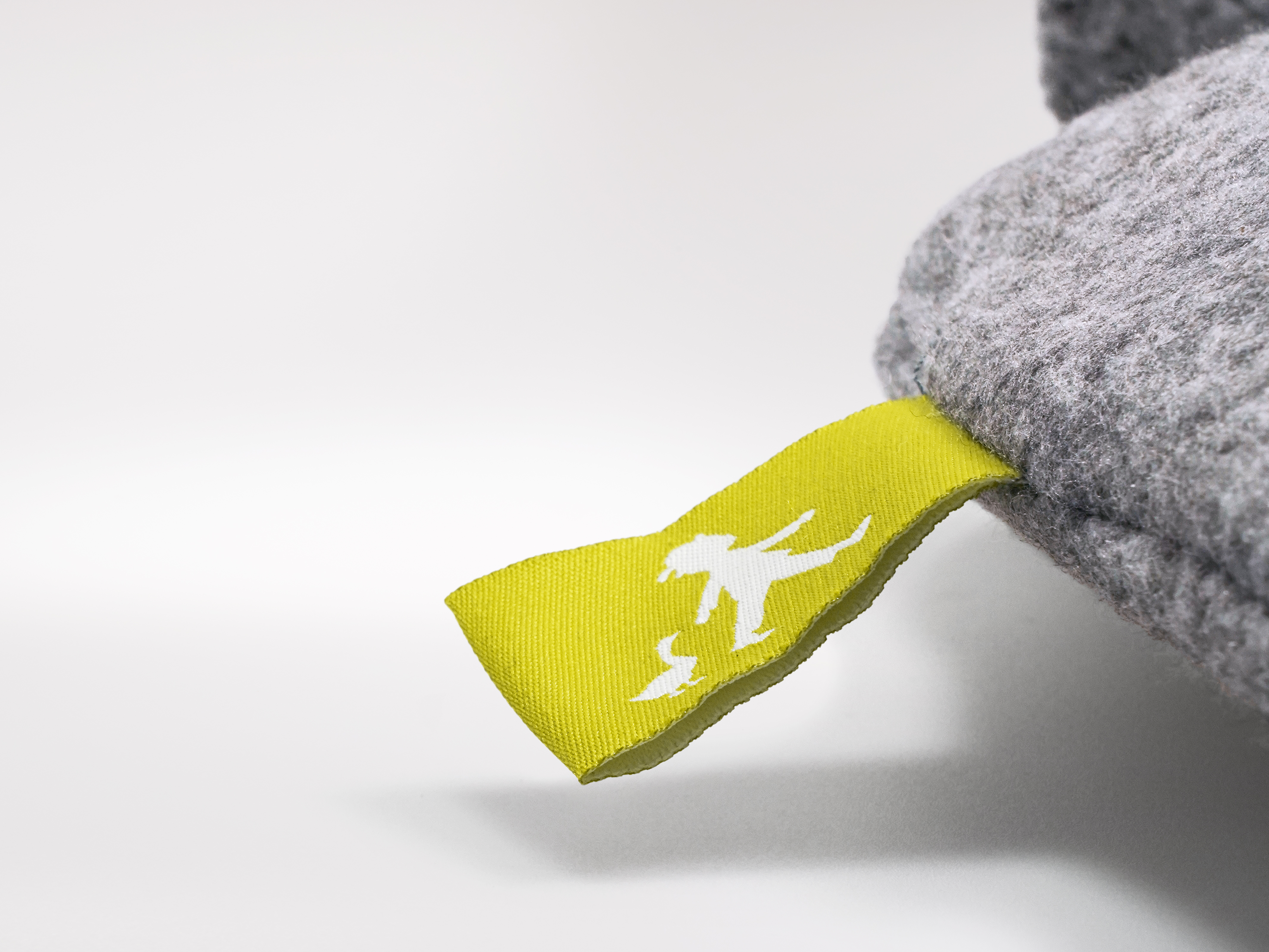 Detailaufnahme des Etiketts und Reißverschlusses einer grauen Wärmflasche mit Maskottchen-Logo in Gelb.