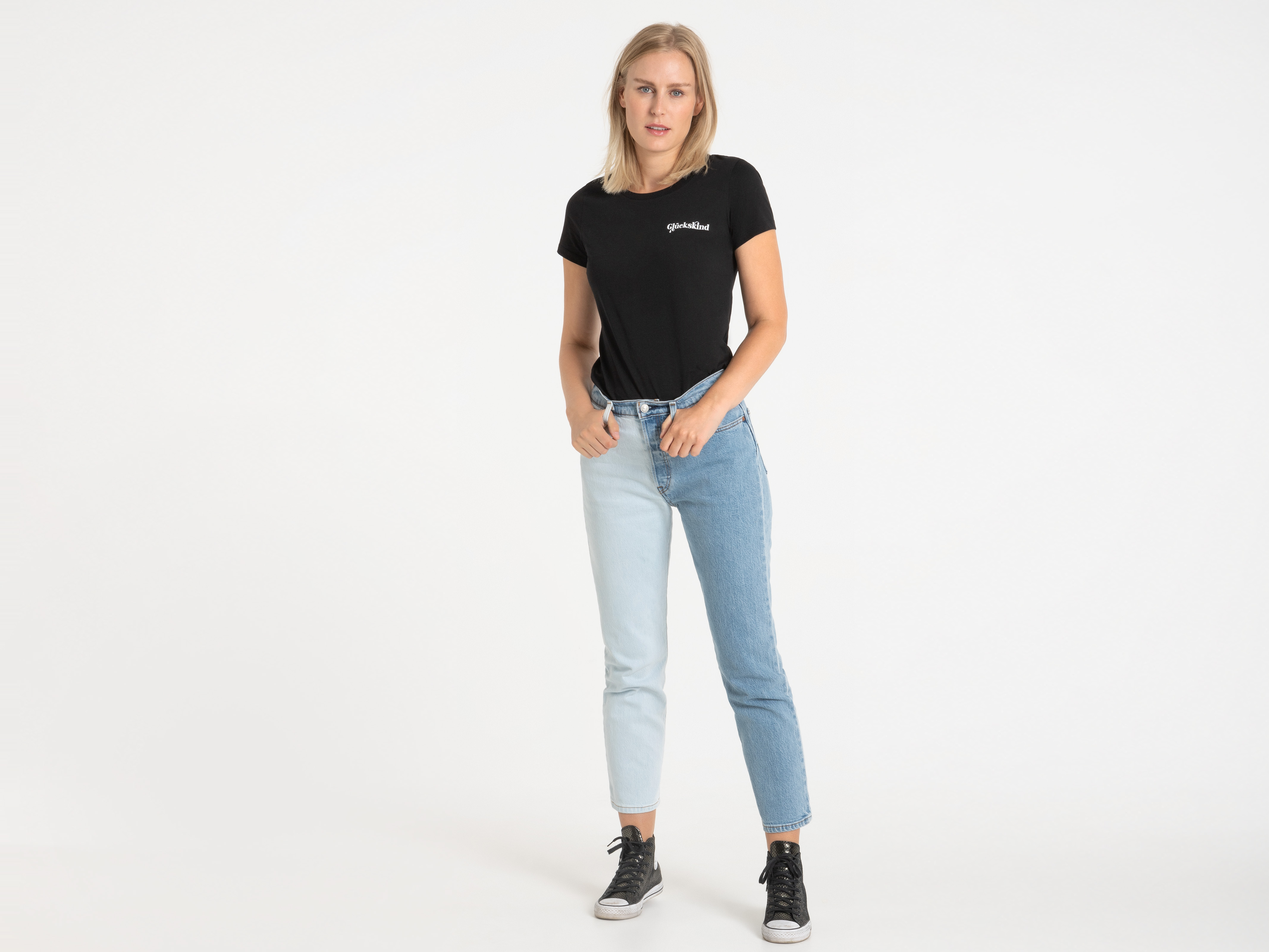 Frau im schwarzen Shirt mit kleinem weißen Logo steht locker mit einer Hand in der Tasche – schlicht und modern.