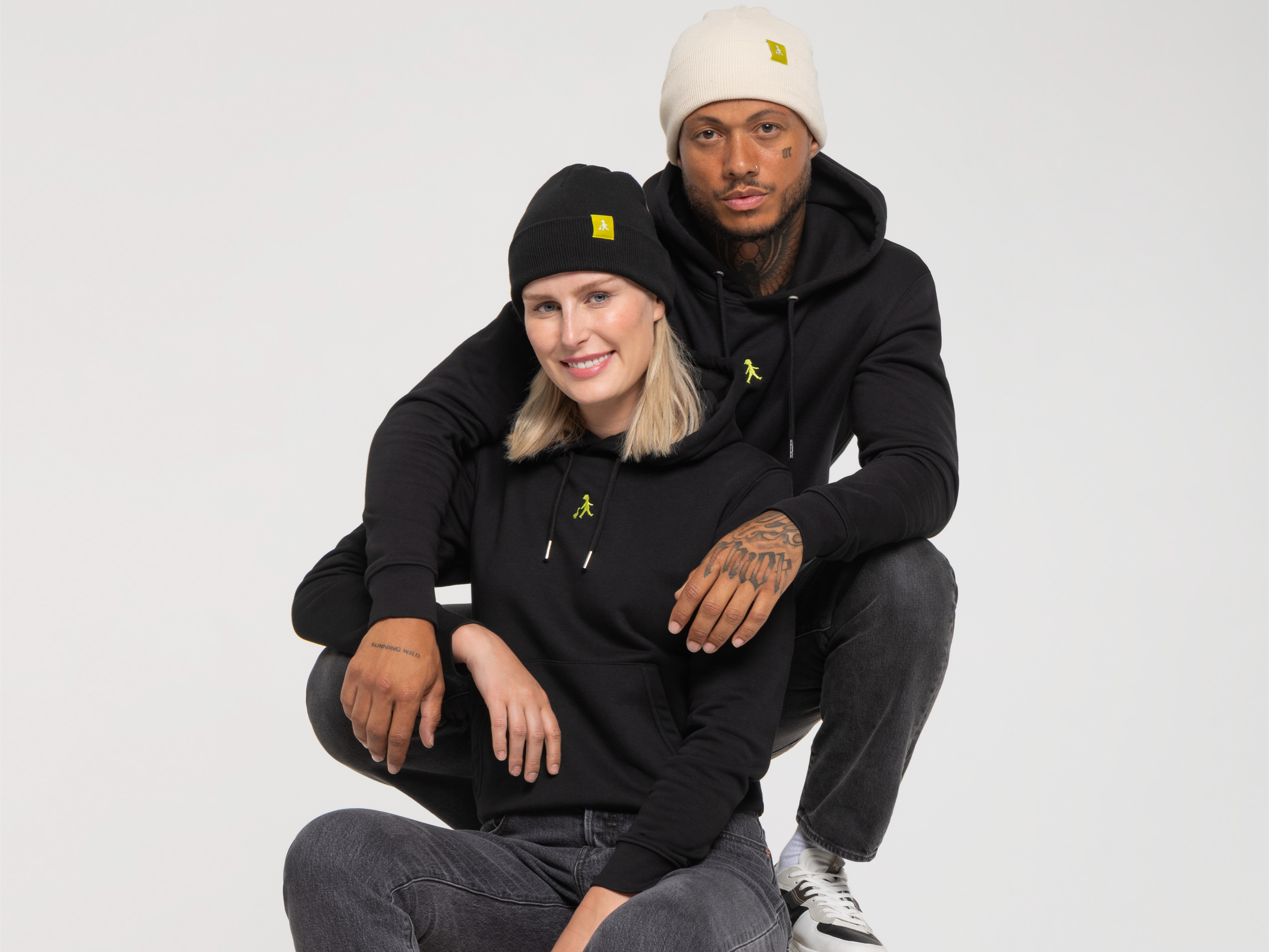 Das Paar sitzt nah beieinander. Beide tragen dunkle Hoodies, die Frau eine schwarze Beanie, der Mann eine helle Mütze mit gelbem Logo.