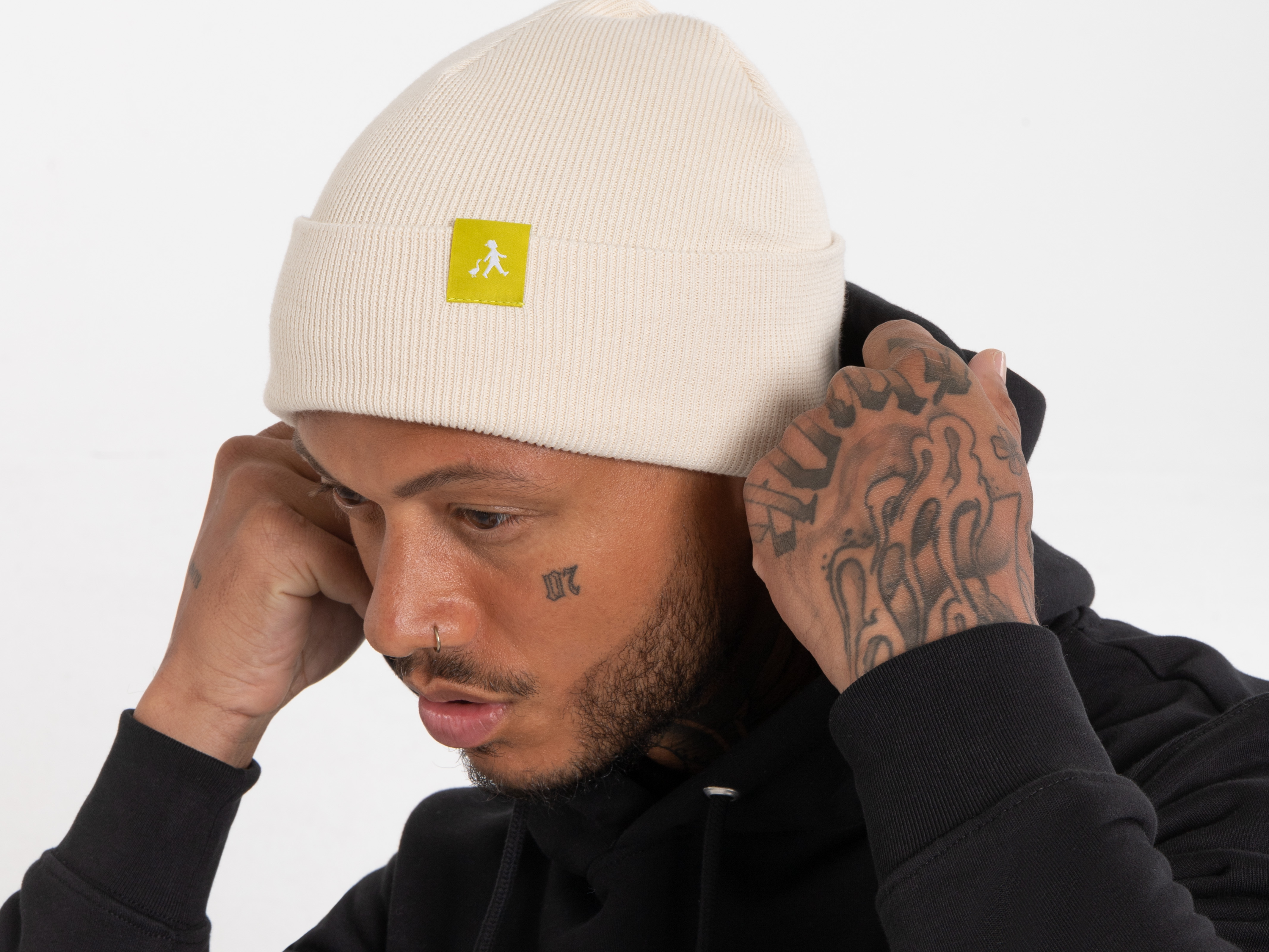 Ein Mann setzt sich eine helle Beanie mit gelbem Label auf. Er trägt einen schwarzen Hoodie, der Blick geht konzentriert zur Seite.