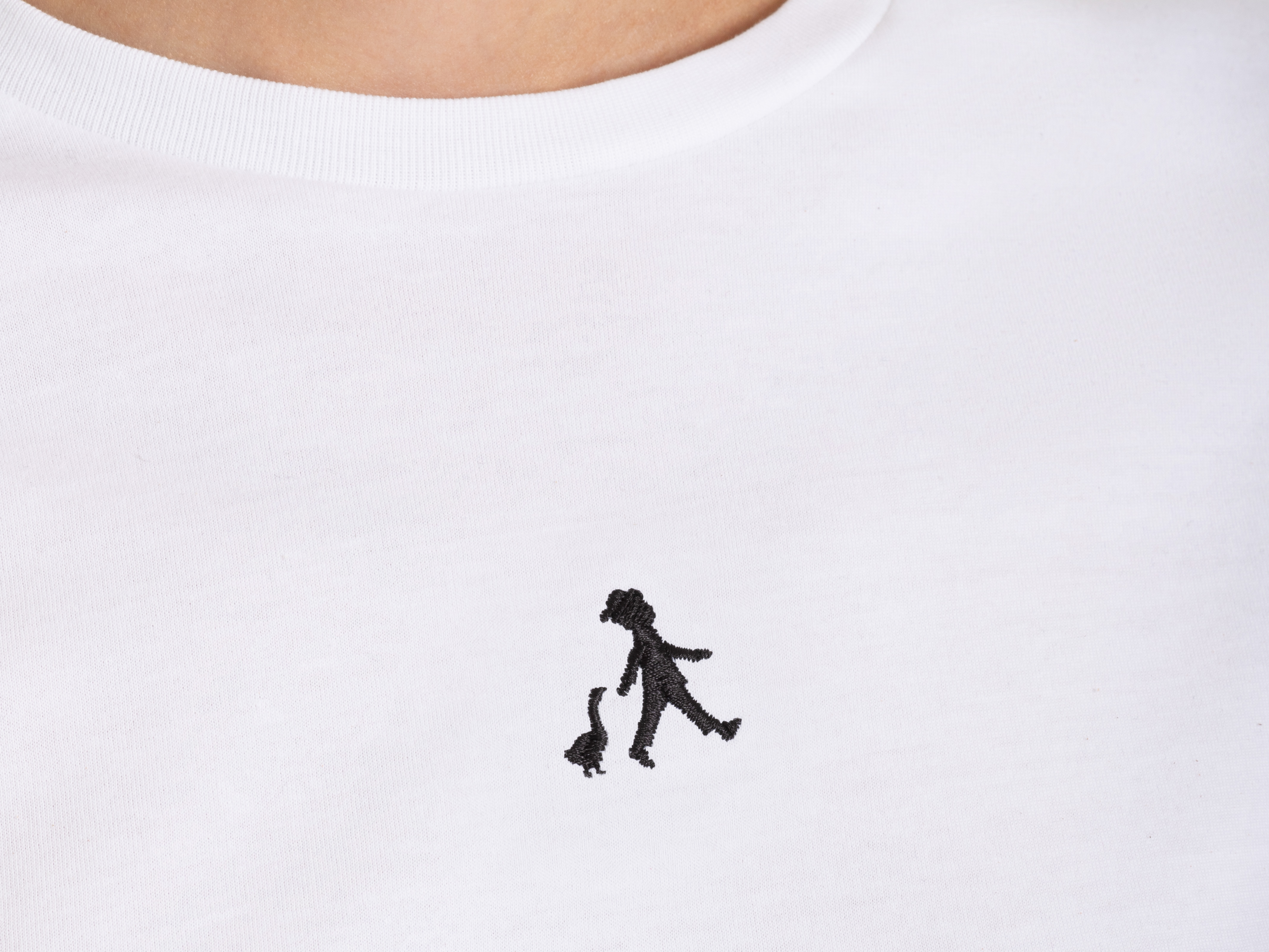 Nahaufnahme des ‚Hans im Glück‘-Logos als schwarze Stickerei auf weißem T-Shirt – dezentes Markendetail