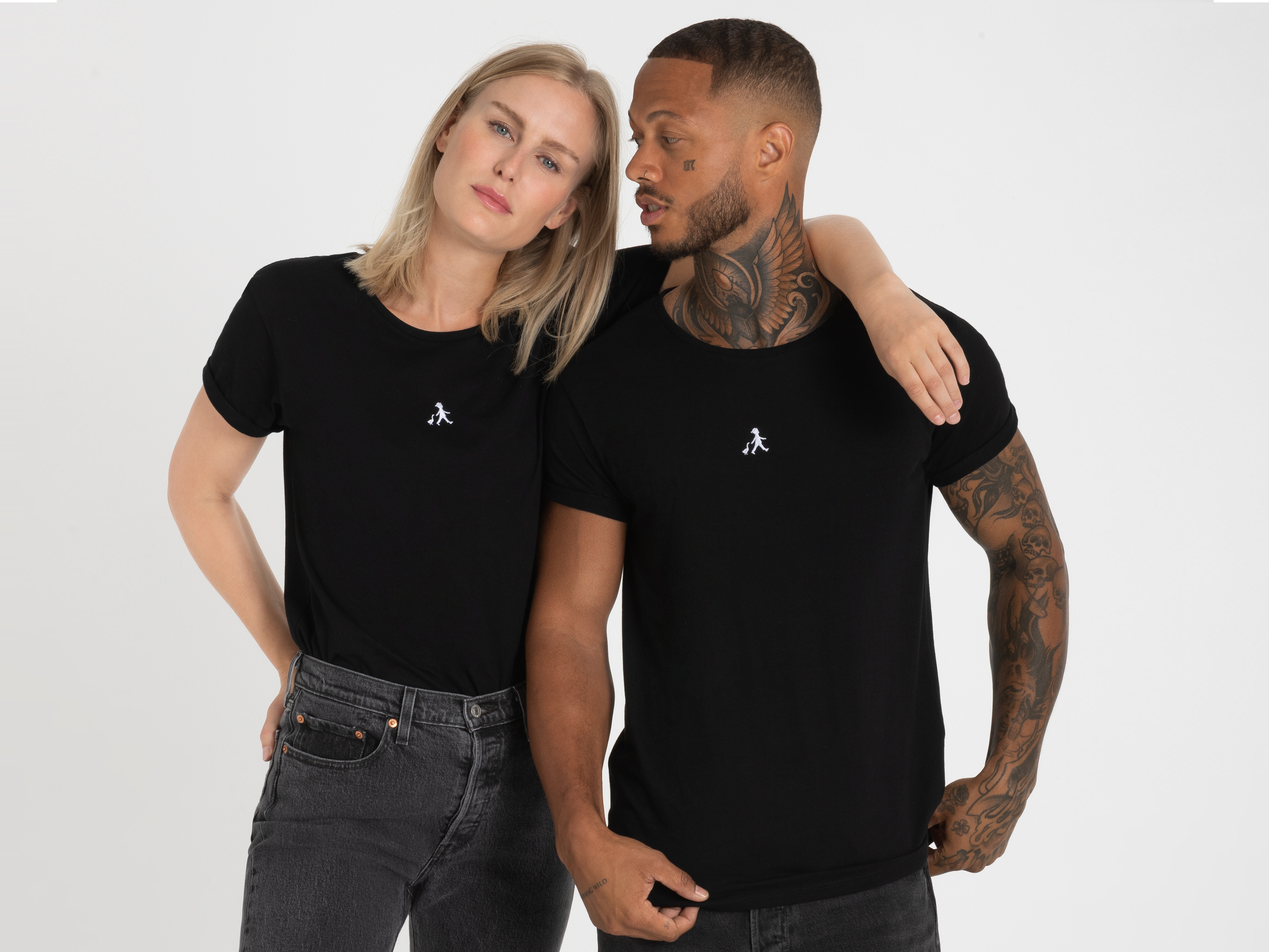 Modisches Duo in schwarzer Kleidung: Die Frau legt den Arm um den Mann, beide stehen locker nebeneinander und wirken entspannt.