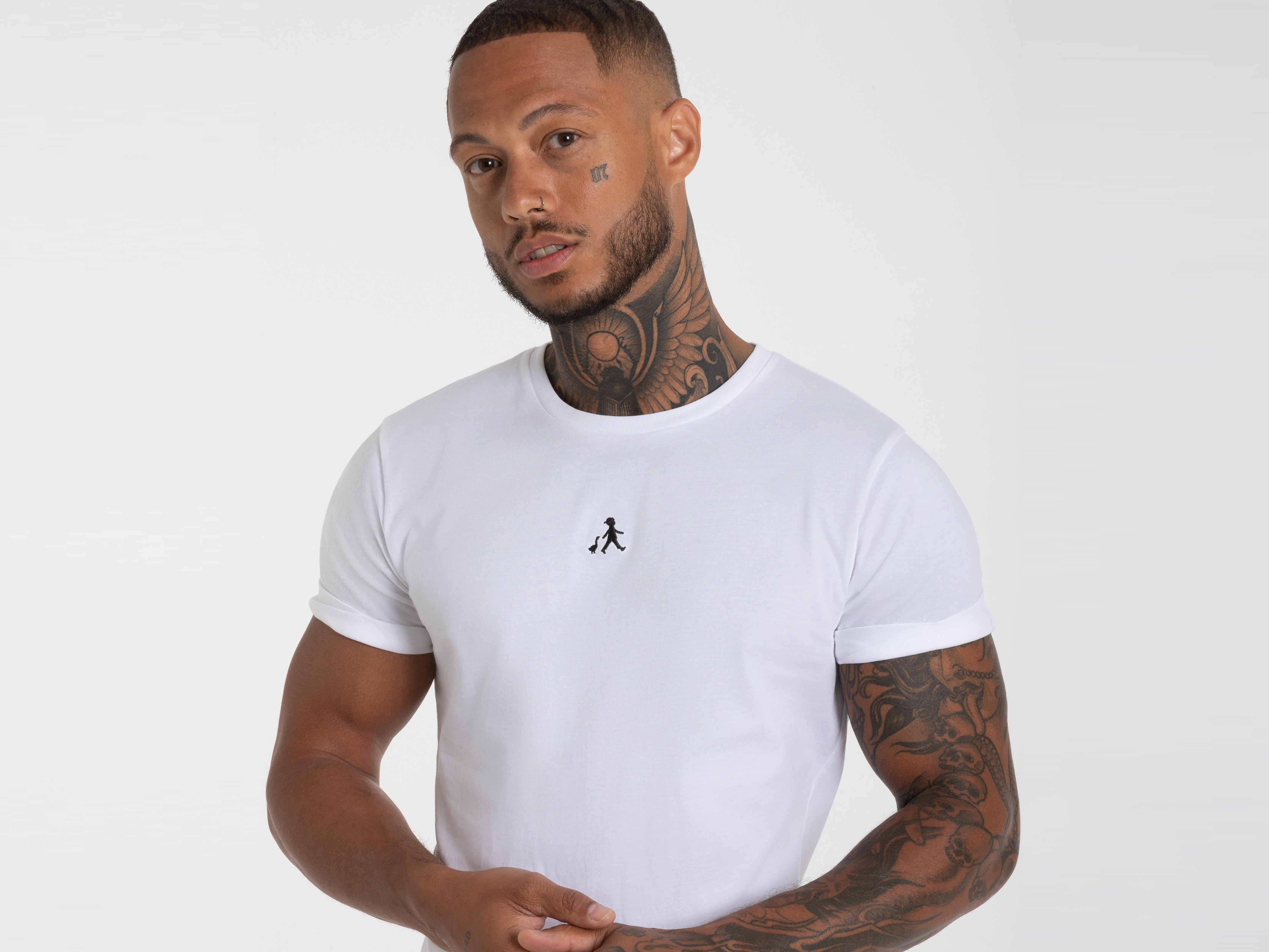 Mann im weißen T-Shirt mit kleinem Logo links auf der Brust – modernes Statement-Shirt mit feinem Detail.