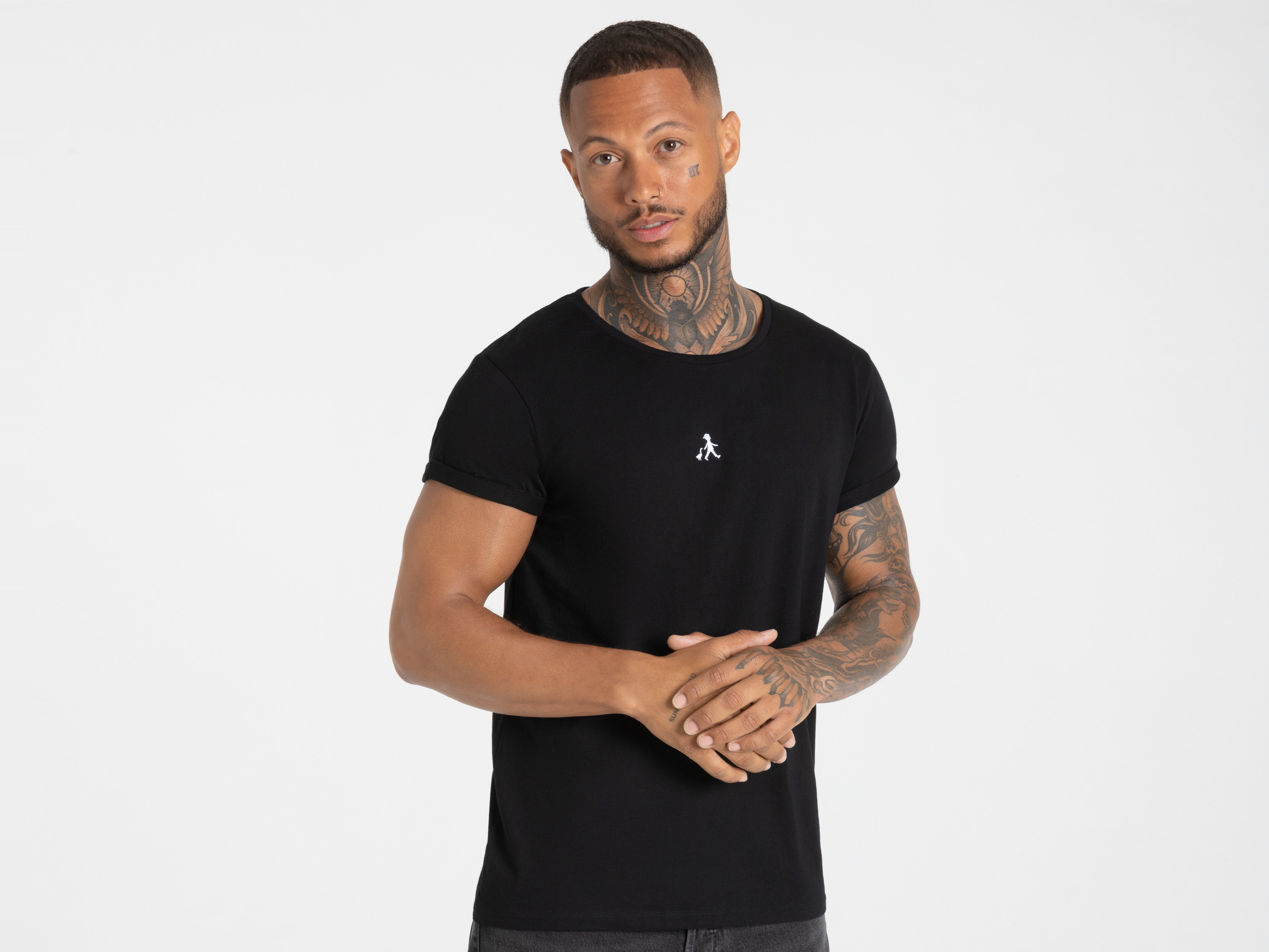 Mann im schwarzen T-Shirt mit Logo verschränkt die Hände – stilvoller Basic-Look.