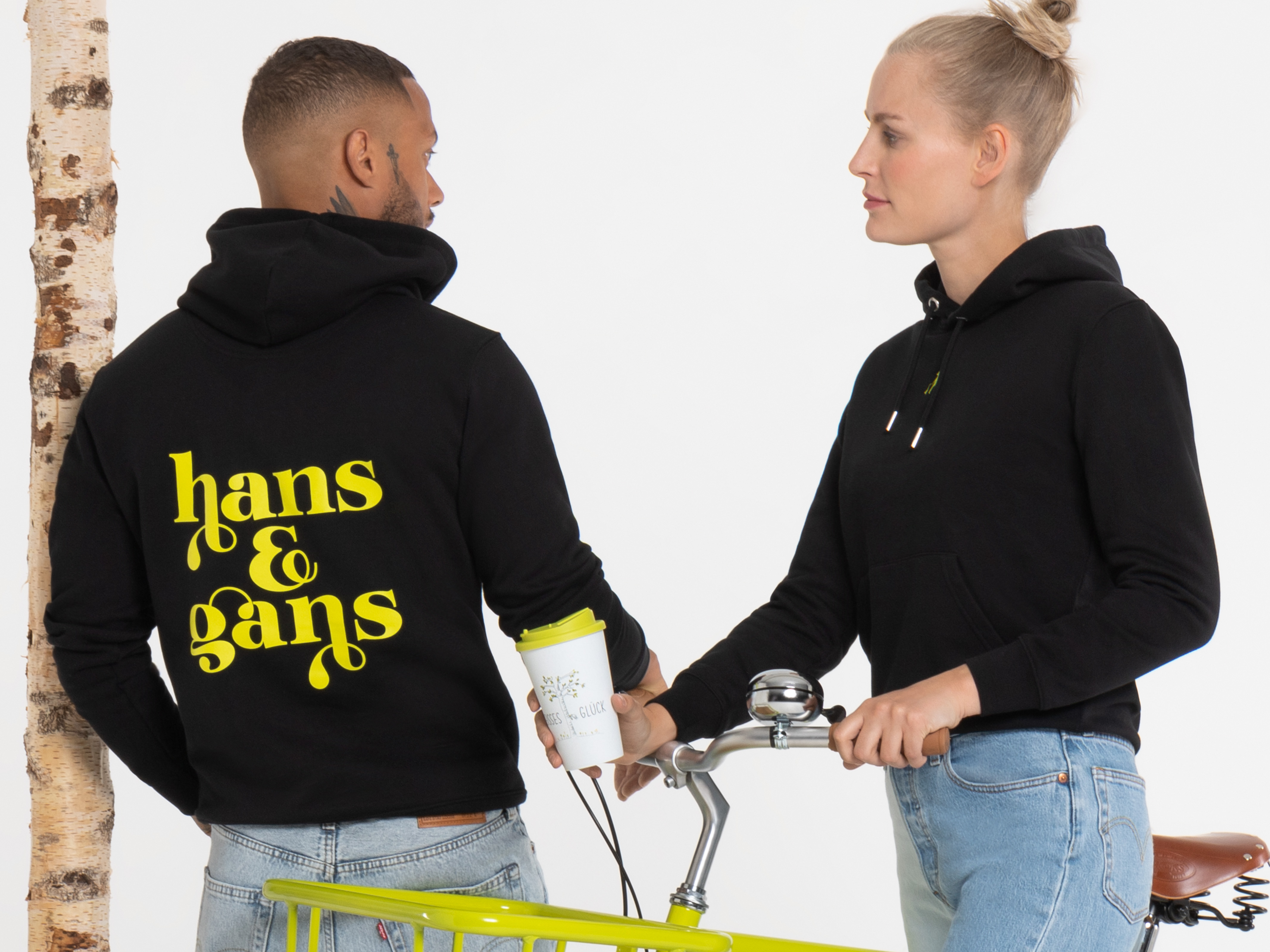 Detailaufnahme des Hoodie-Rückens: gelber „hans & gans“-Print auf schwarzem Stoff, daneben der Träger leicht im Profil sichtbar, vor weißem Hintergrund.