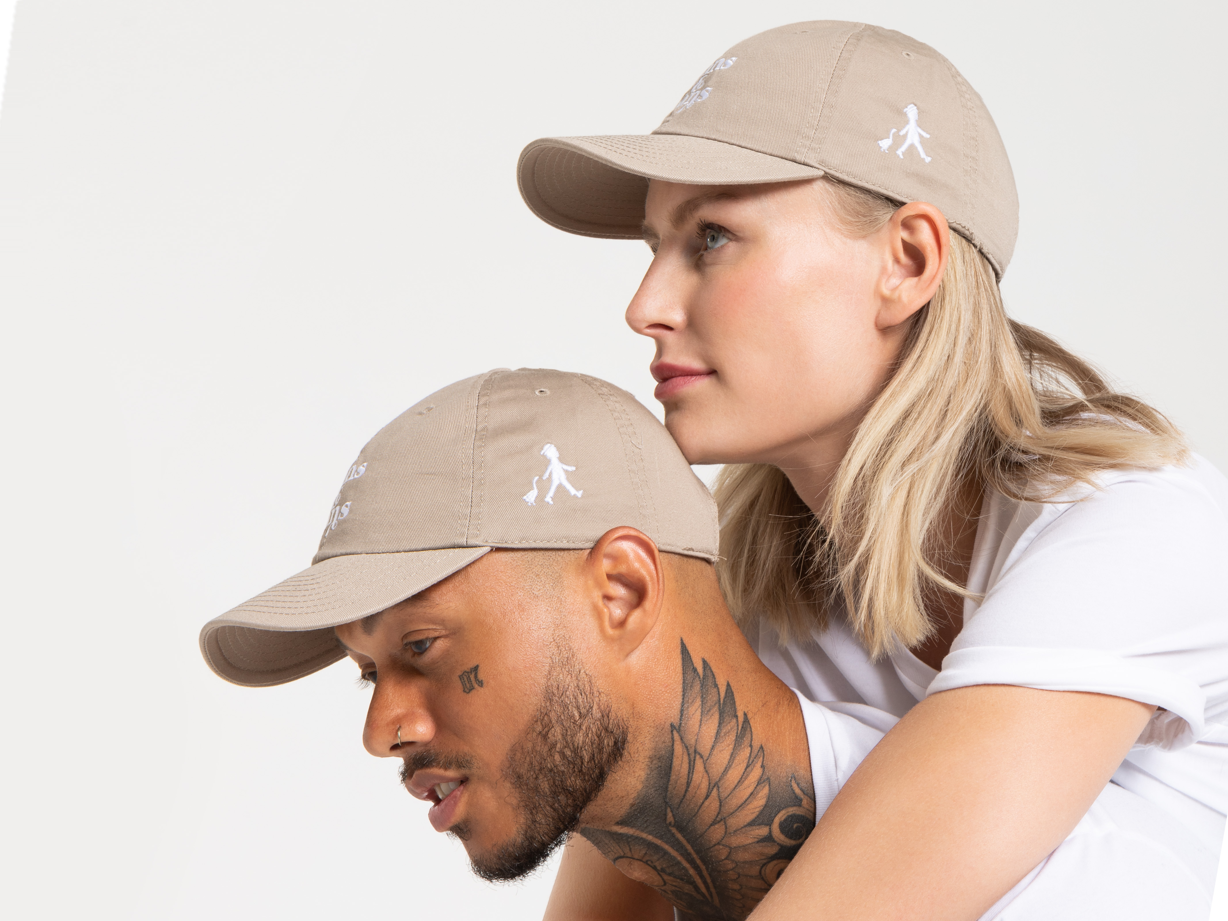 Die Frau blickt ruhig nach vorne, der Mann schaut leicht nach unten. Beide tragen beigefarbene Caps mit Logo, schlichtes weißes Oberteil, klare Produktpräsentation.