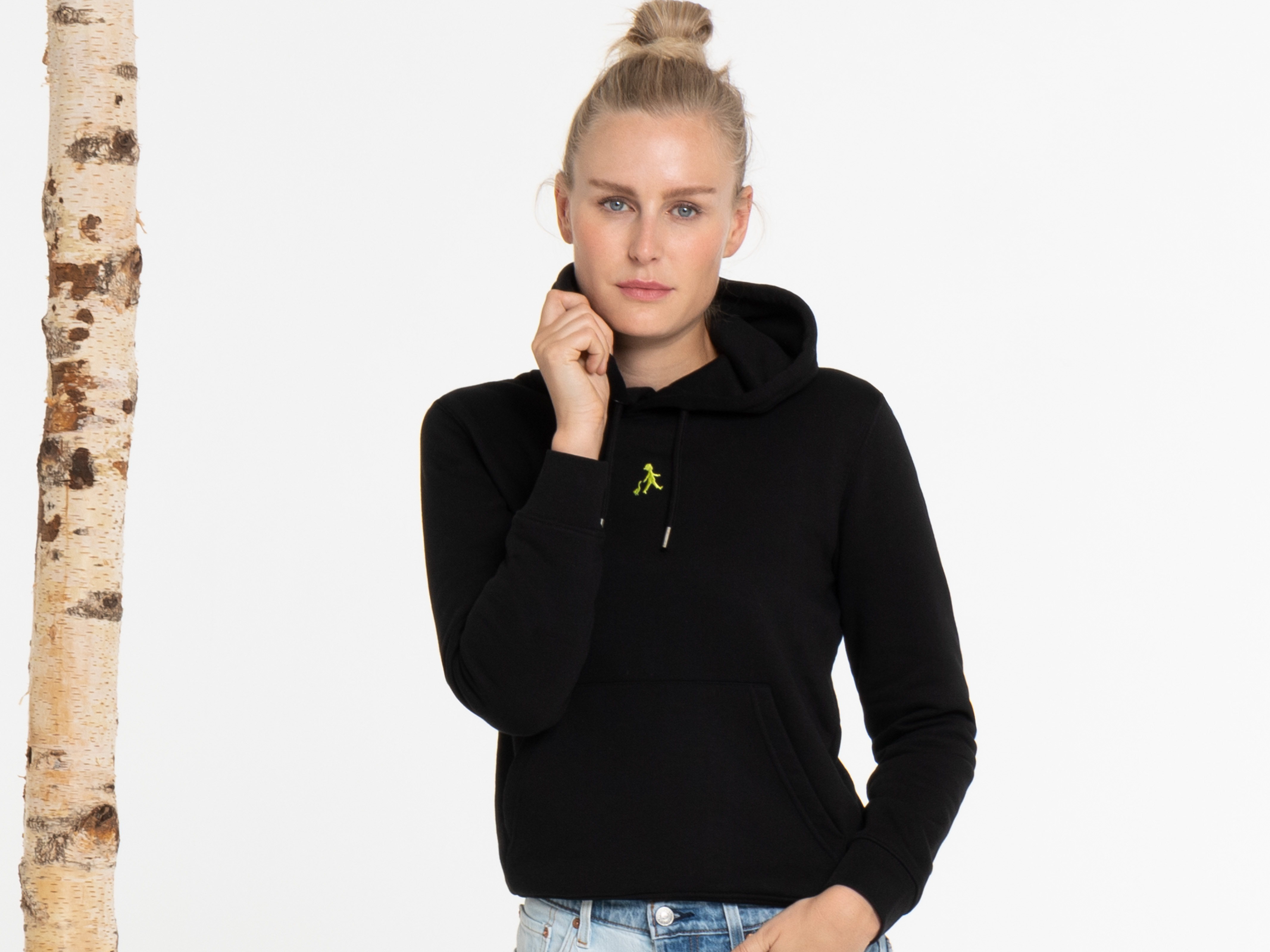 Die Frau blickt ruhig in die Kamera, trägt einen schwarzen Hoodie mit Kapuze, hält den Kragen leicht mit einer Hand – Porträt-Stimmung, urbaner Stil.