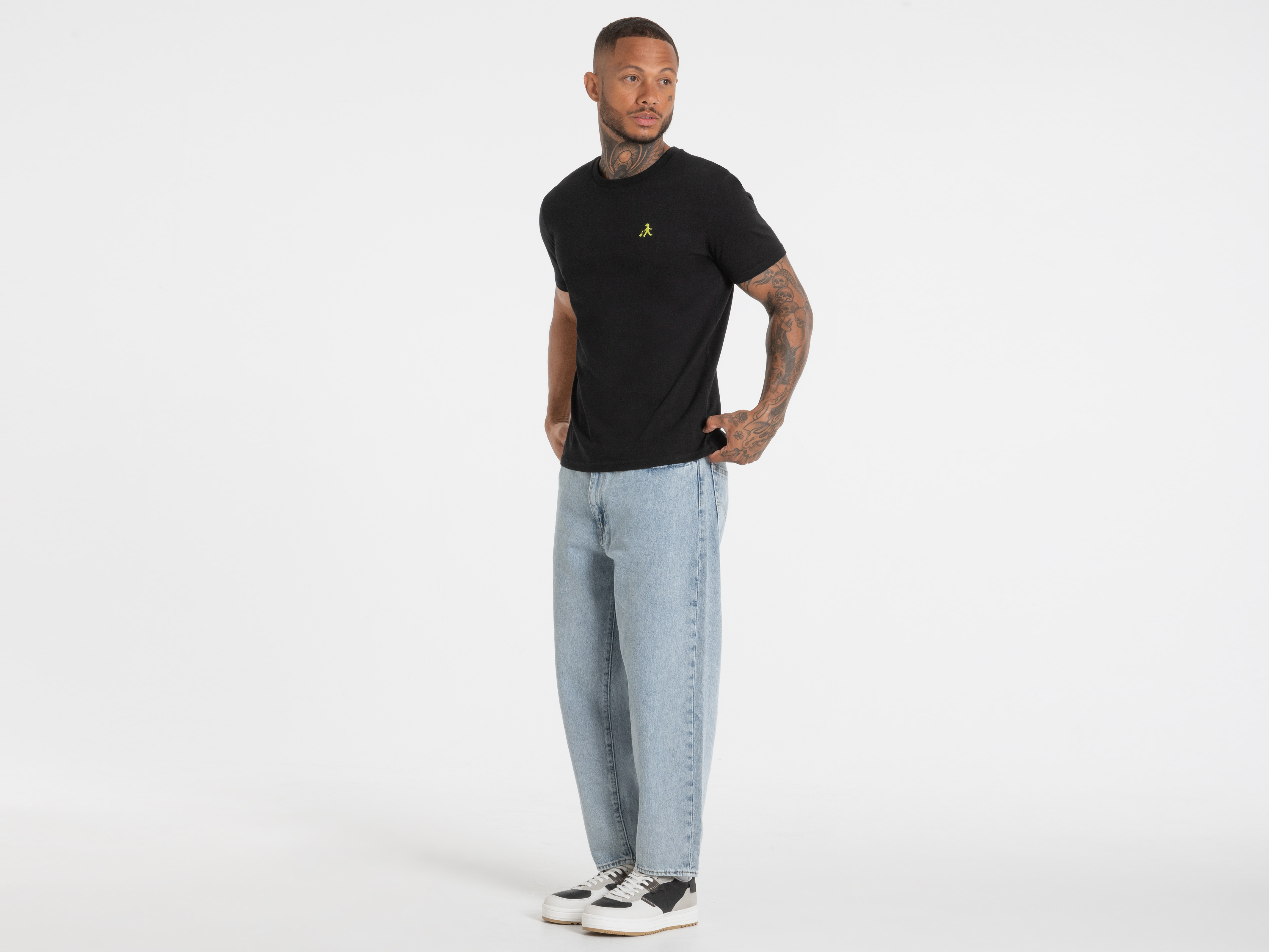 Mann steht frontal im schwarzen T-Shirt mit gelbem Logo – schlichtes Shirt mit Statement-Charakter.